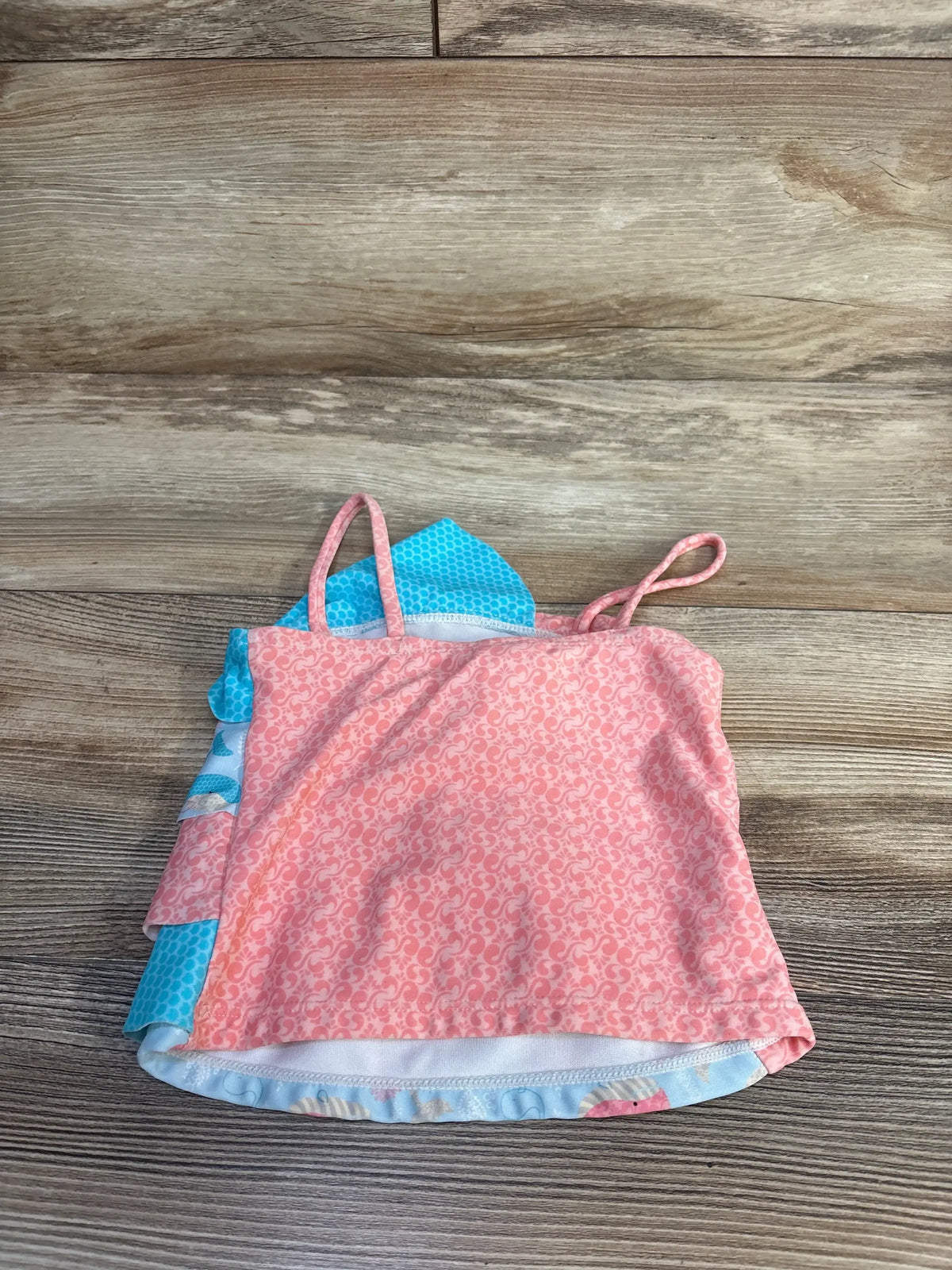 Front view of Kiko & Max tank swim top with pink floral overlay, blue patterned panels, thin straps, and ruffled layers on wood background