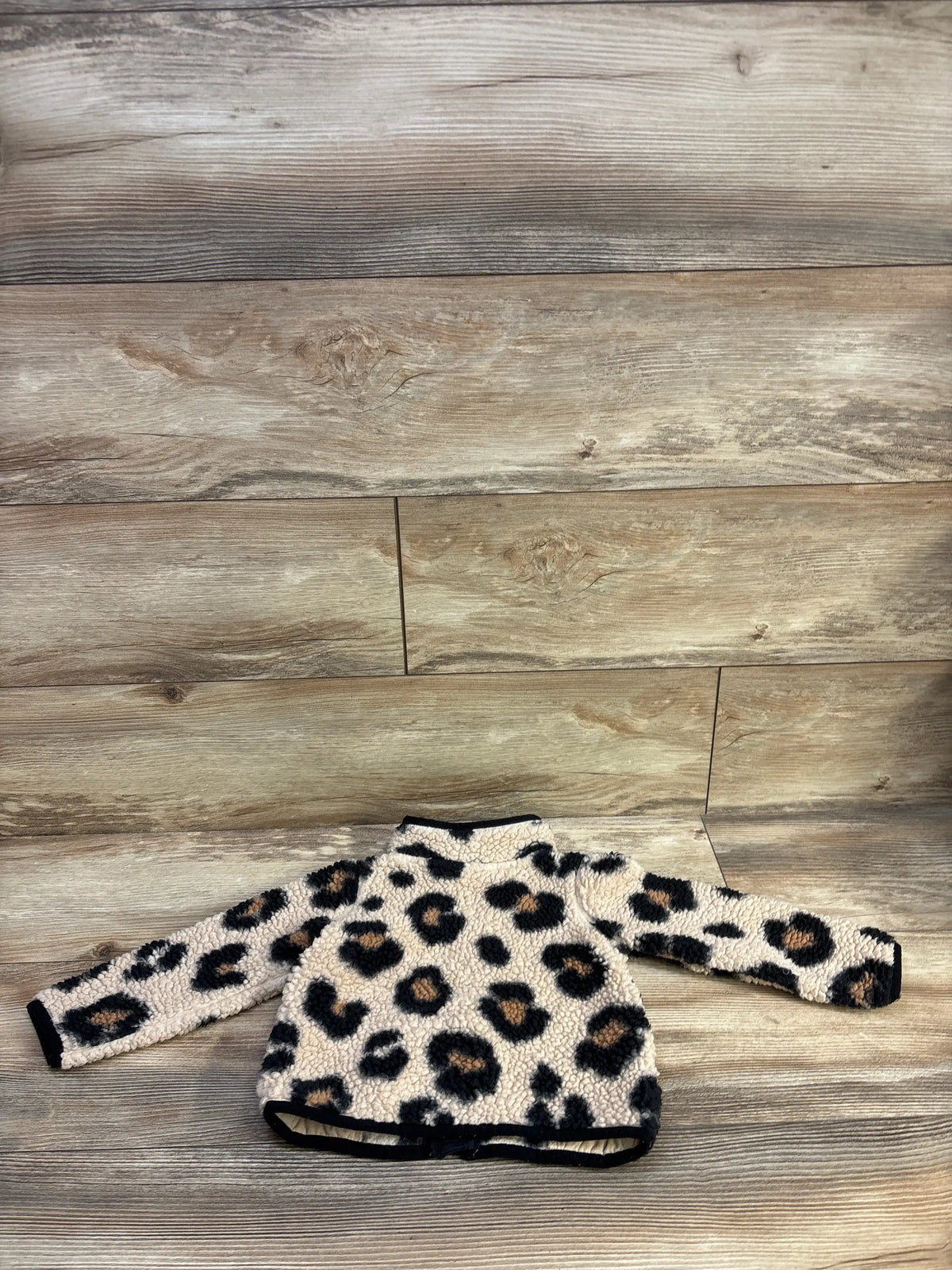 Flat lay of leopard-print sherpa toddler jacket showcasing fuzzy sherpa fabric and black trim on wood plank background