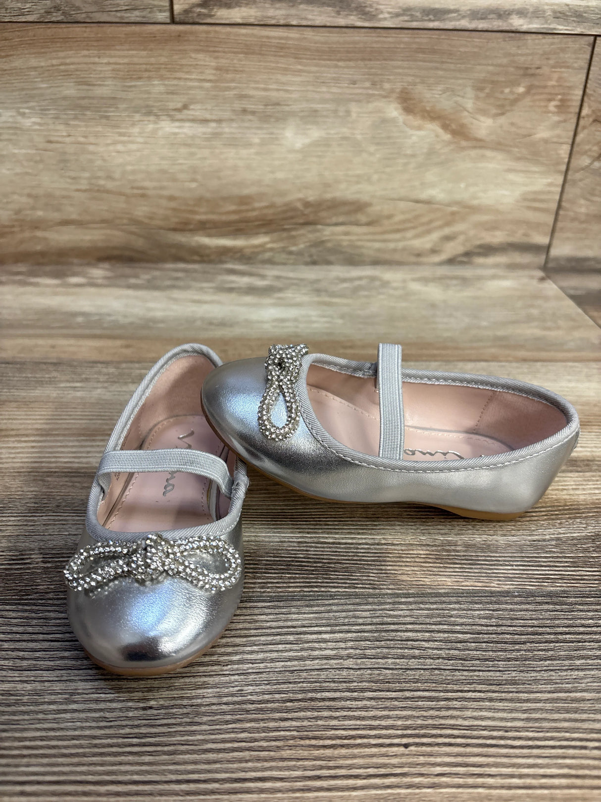 Silver girls' dress shoes with rhinestone bows on wood background