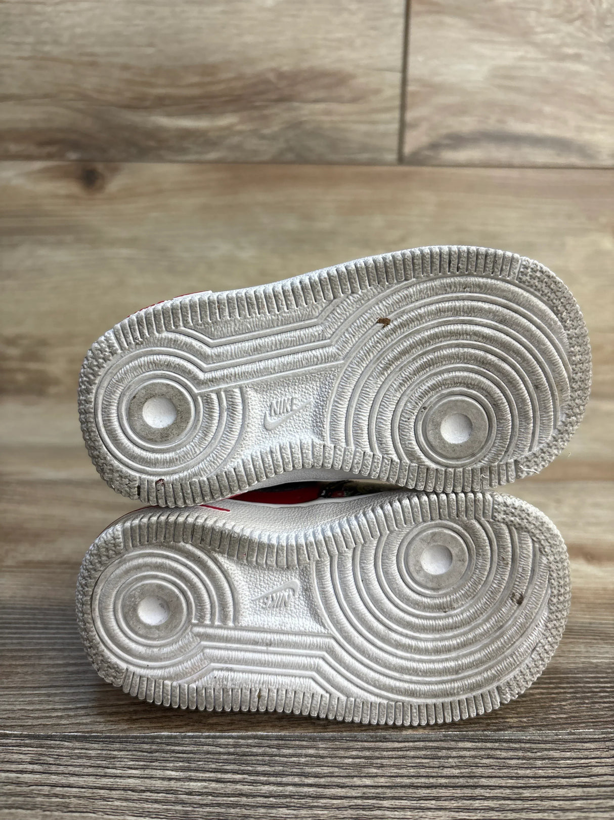 Sole view of Nike Force 1 TD Strawberry Banana sneakers size 5c showing white circular tread pattern and Nike branding on wood plank floor