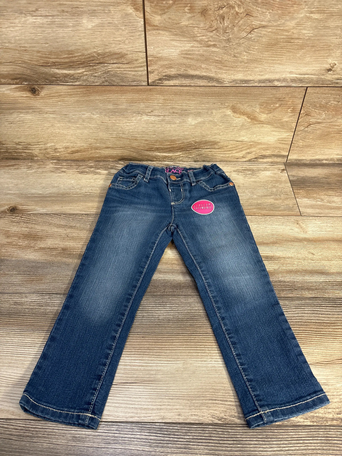 Front view of Children’s Place skinny jeans showcasing blue denim, five pockets, and button closure on a wood background