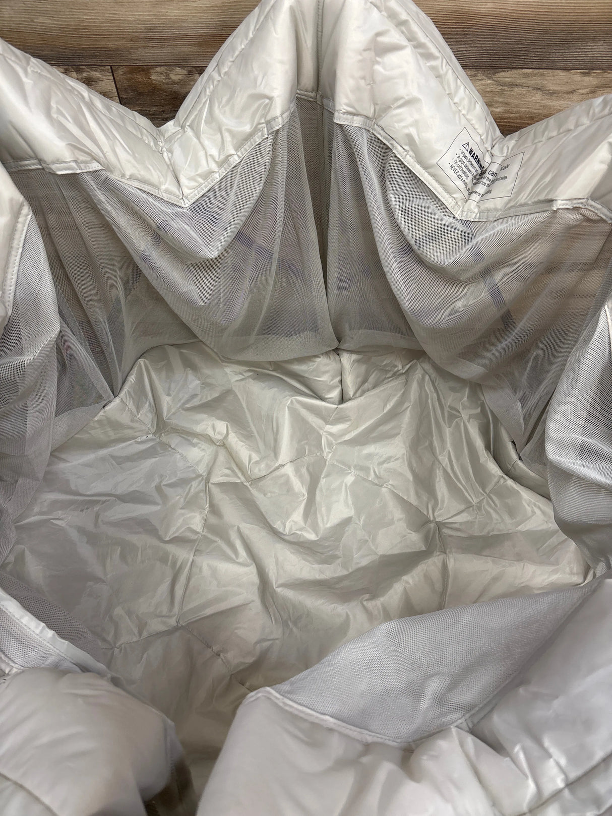 Empty white mesh laundry hamper with fabric lining on a wooden floor