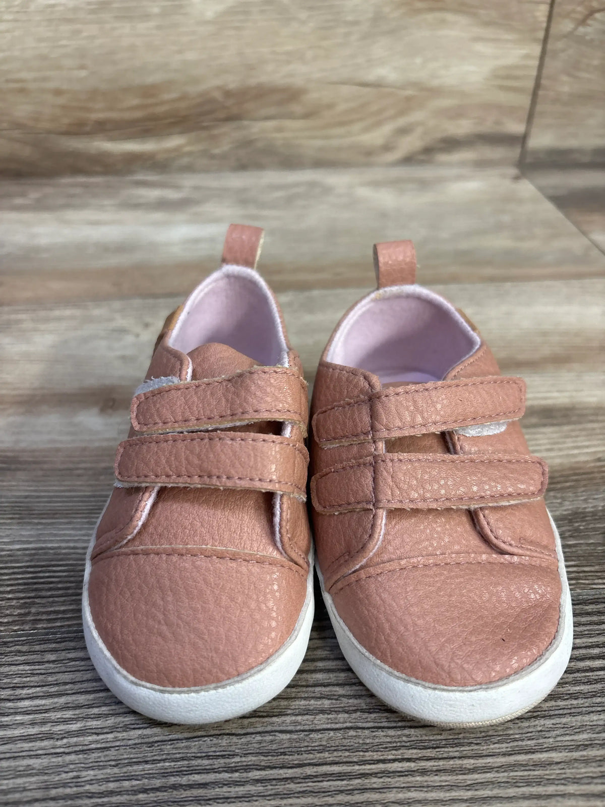 Front view of pink Rokment non-slip crib shoes showing double straps, pull tabs, and white soles on a wood floor