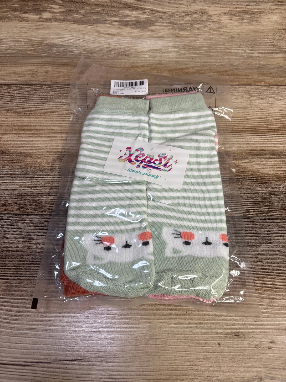 Front view of XEPST three-pack toddler leg warmers, green-and-white striped with animal faces in packaging