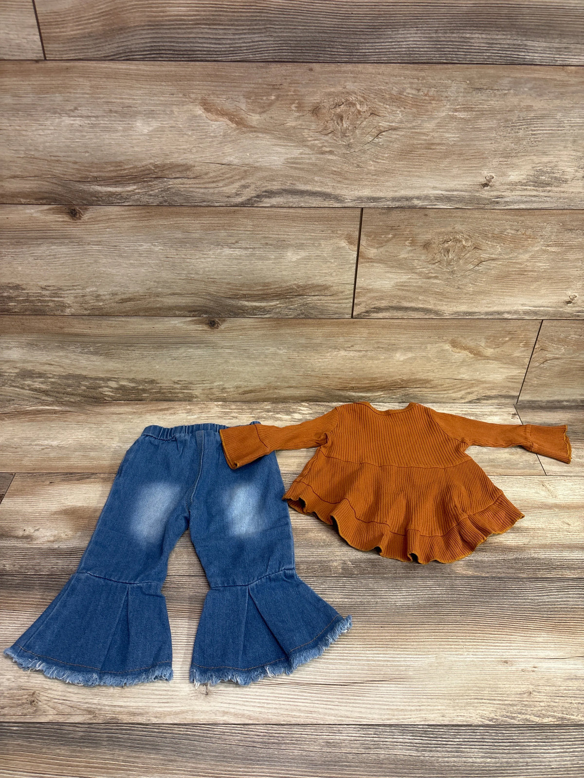 Top-down view of Kucnuzki two-piece outfit showcasing a ribbed brown ruffle top and blue bell-bottom jeans on wood-look flooring