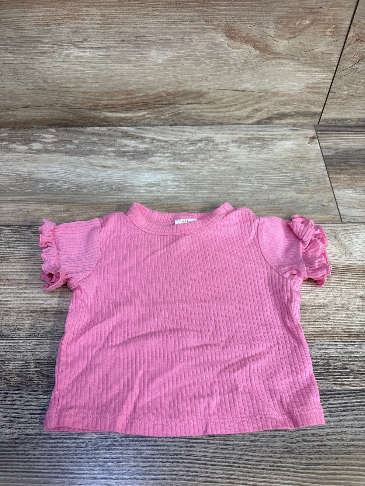 Front view of Cat and Jack pink ribbed shirt showcasing ruffled short sleeves with a wood-look floor background
