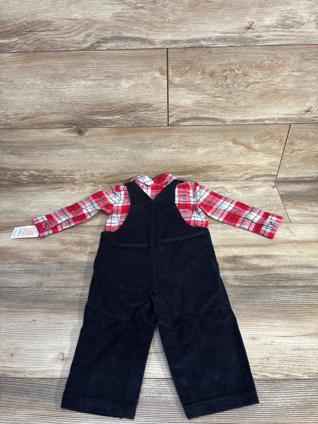 Kids' black corduroy overalls with red plaid long sleeve shirt, laid on wood floor