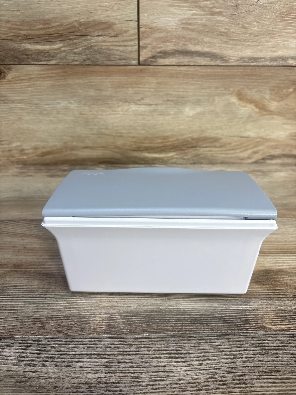 Front view of Ubbi grey wipes dispenser showcasing its lidded design on a wood surface