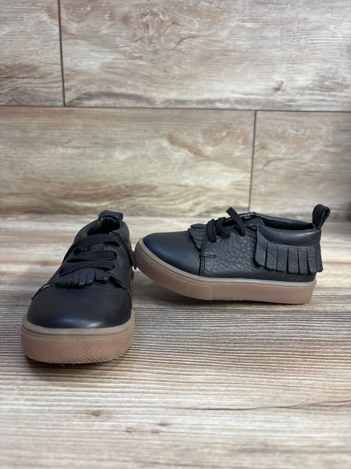 Black toddler fringe sneakers with tan soles on wood floor