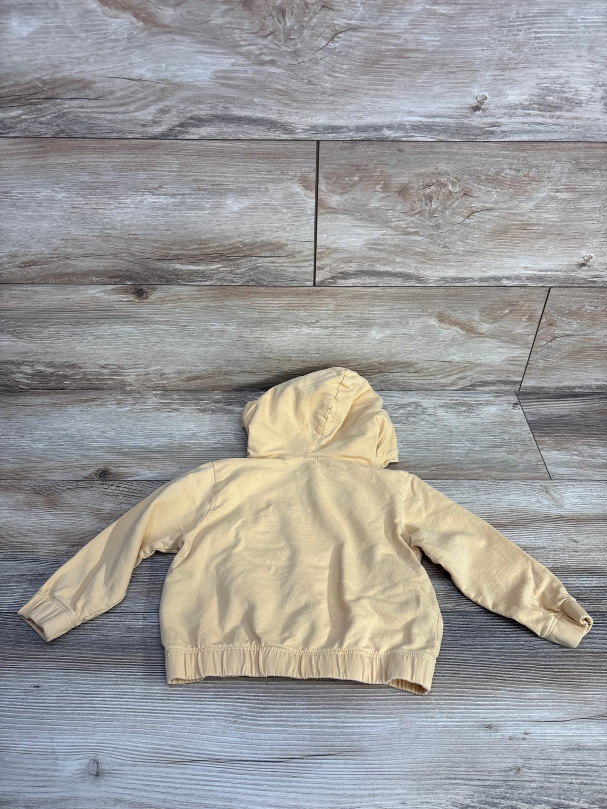 Beige toddler hoodie laid flat on wood floor, back view, casual kids clothing