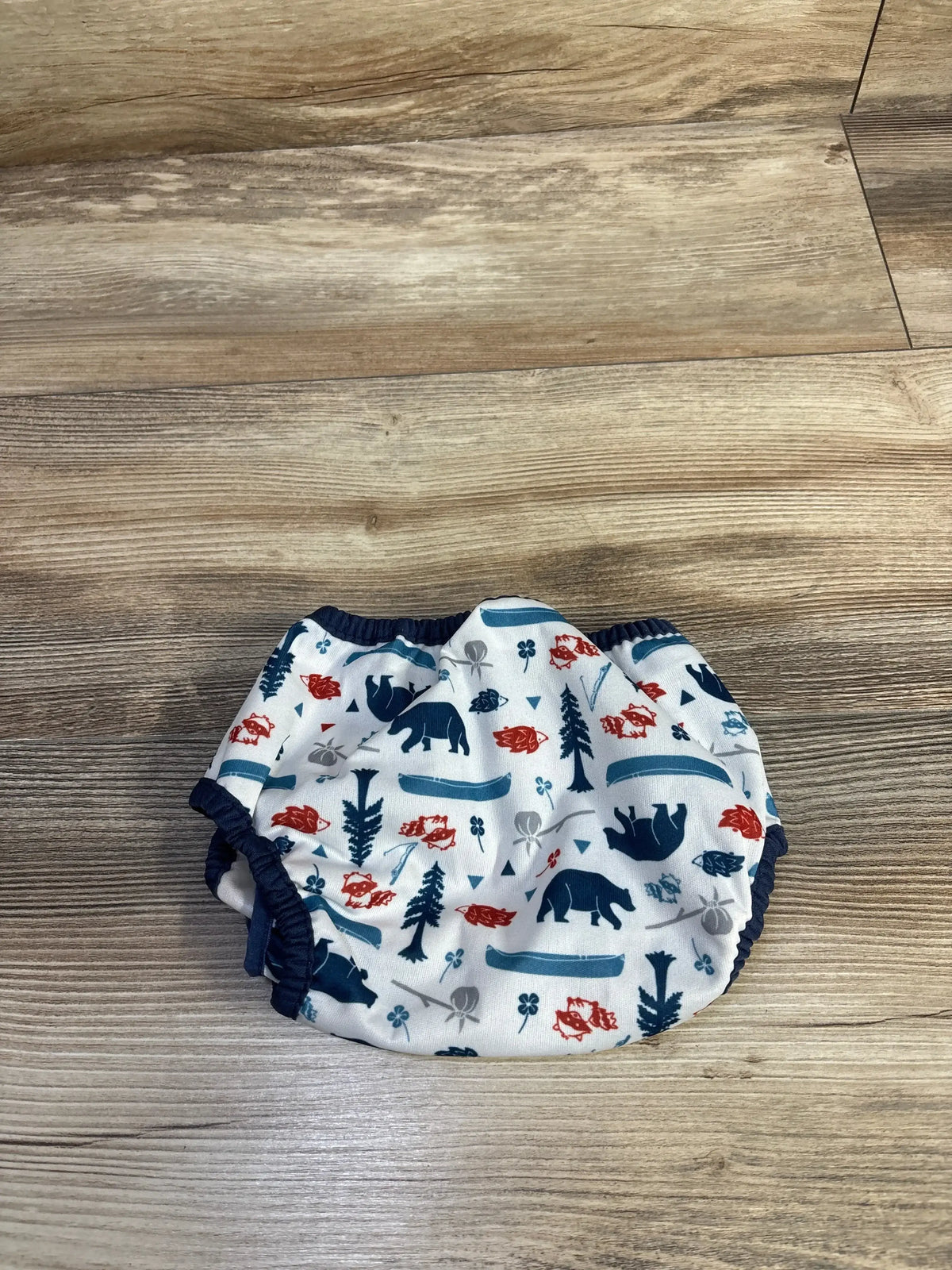 Top-down view of Thirsties swim diaper white with navy trim, bear and canoe print, elastic leg openings on wood floor