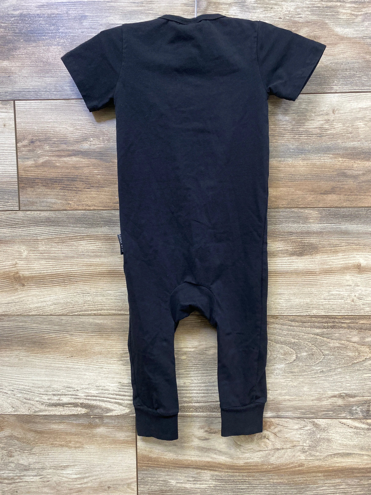 Back view of black short-sleeve toddler romper on wooden floor, children's clothing
