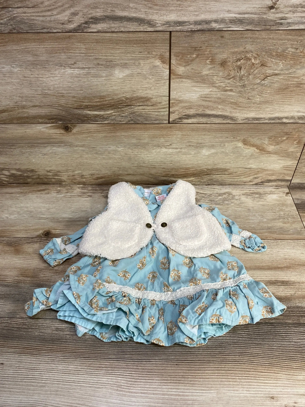 Blue floral baby dress with white plush vest on wooden background, toddler clothing