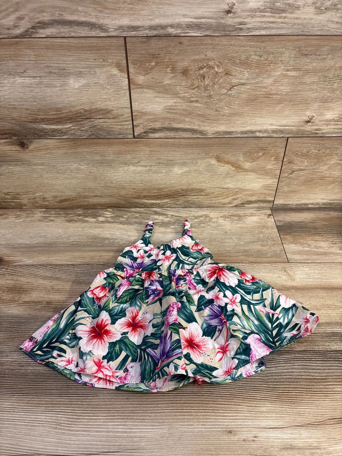 Flat lay of sleeveless baby dress size 3M showcasing green tropical hibiscus print and gathered waist on wood floor background