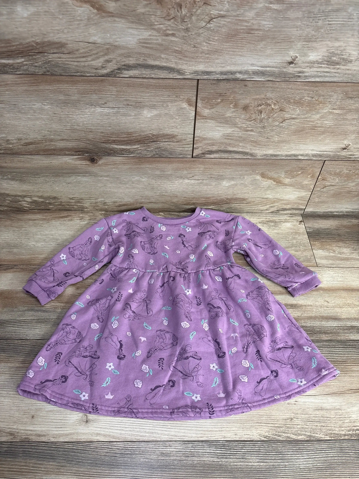 Flat lay of lilac Disney Princess sweatshirt dress (5T) showing long sleeves, ruched waist and floral print on wood floor