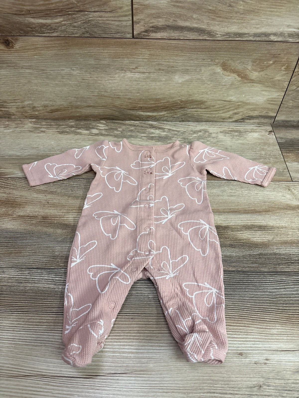 Front view of Carter’s waffle knit snap sleeper showcasing pink fabric, white butterfly print, long sleeves, and snap closures on a wood background