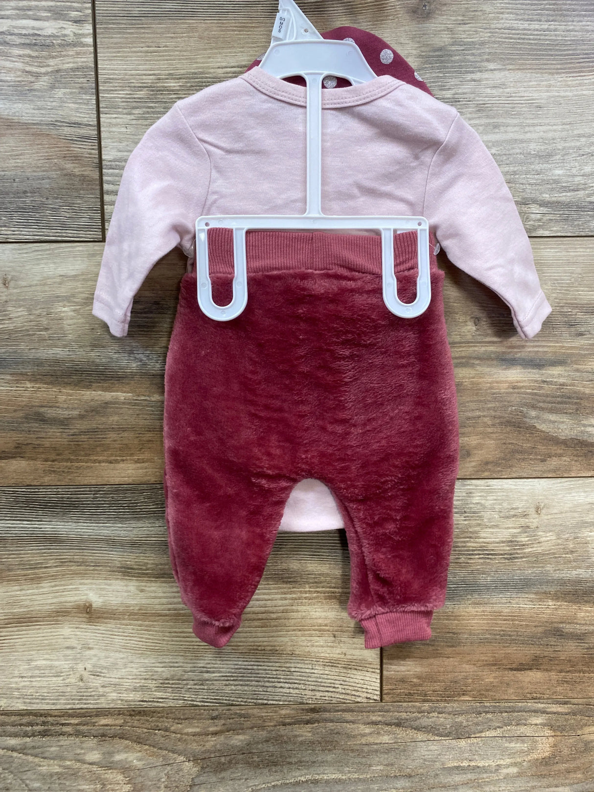 Pink and maroon baby romper on hanger, fleece pants, wooden background