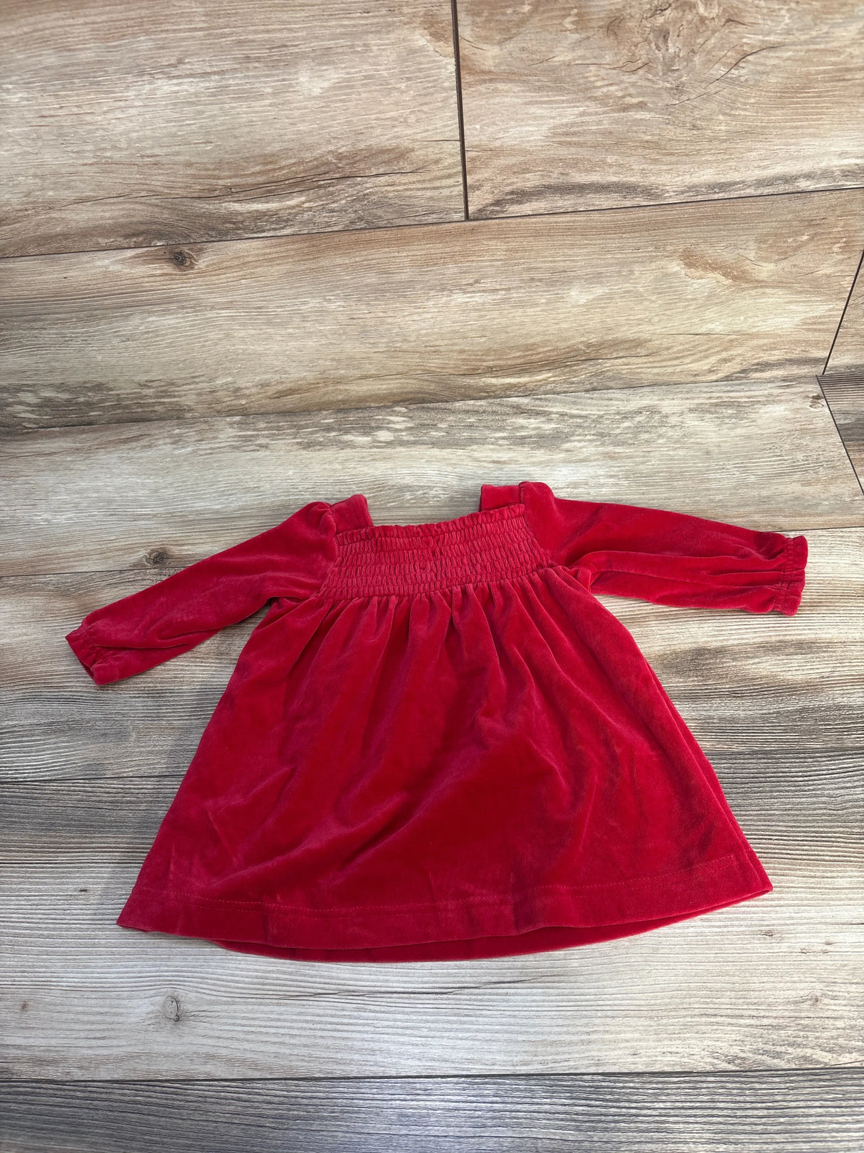 Red velvet long-sleeve baby dress laid flat on wooden floor