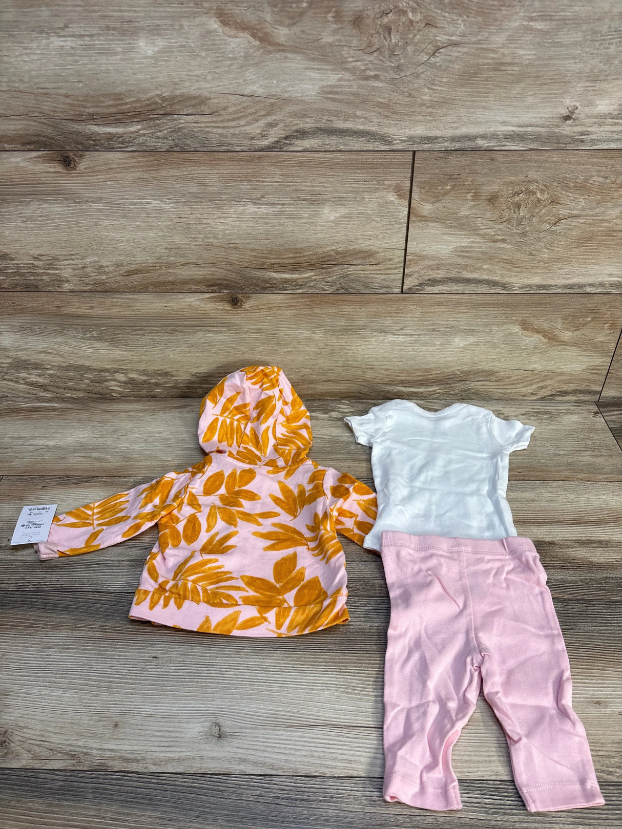 Flat lay of 3pc floral jacket set size 3M with yellow leaf hooded jacket, white onesie and pink leggings on wood floor