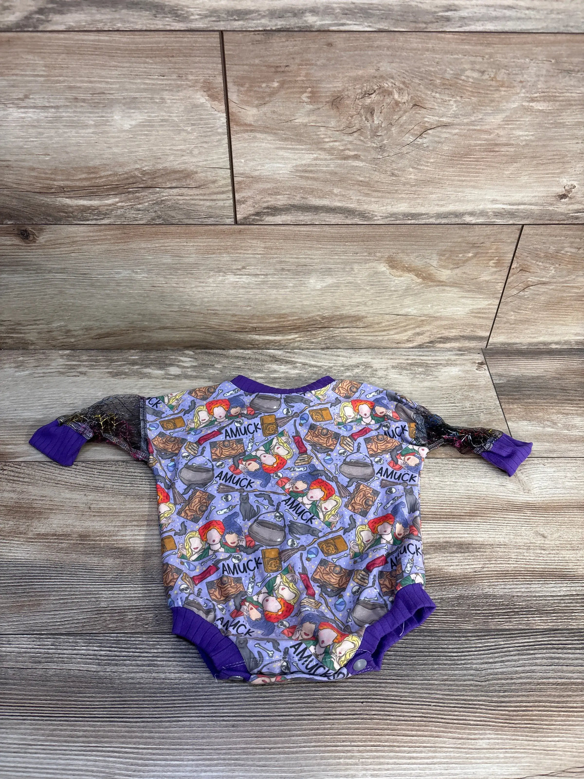 Front view of a purple Hocus Pocus bubble romper showcasing its allover print and bubble hem on a wood-grain background