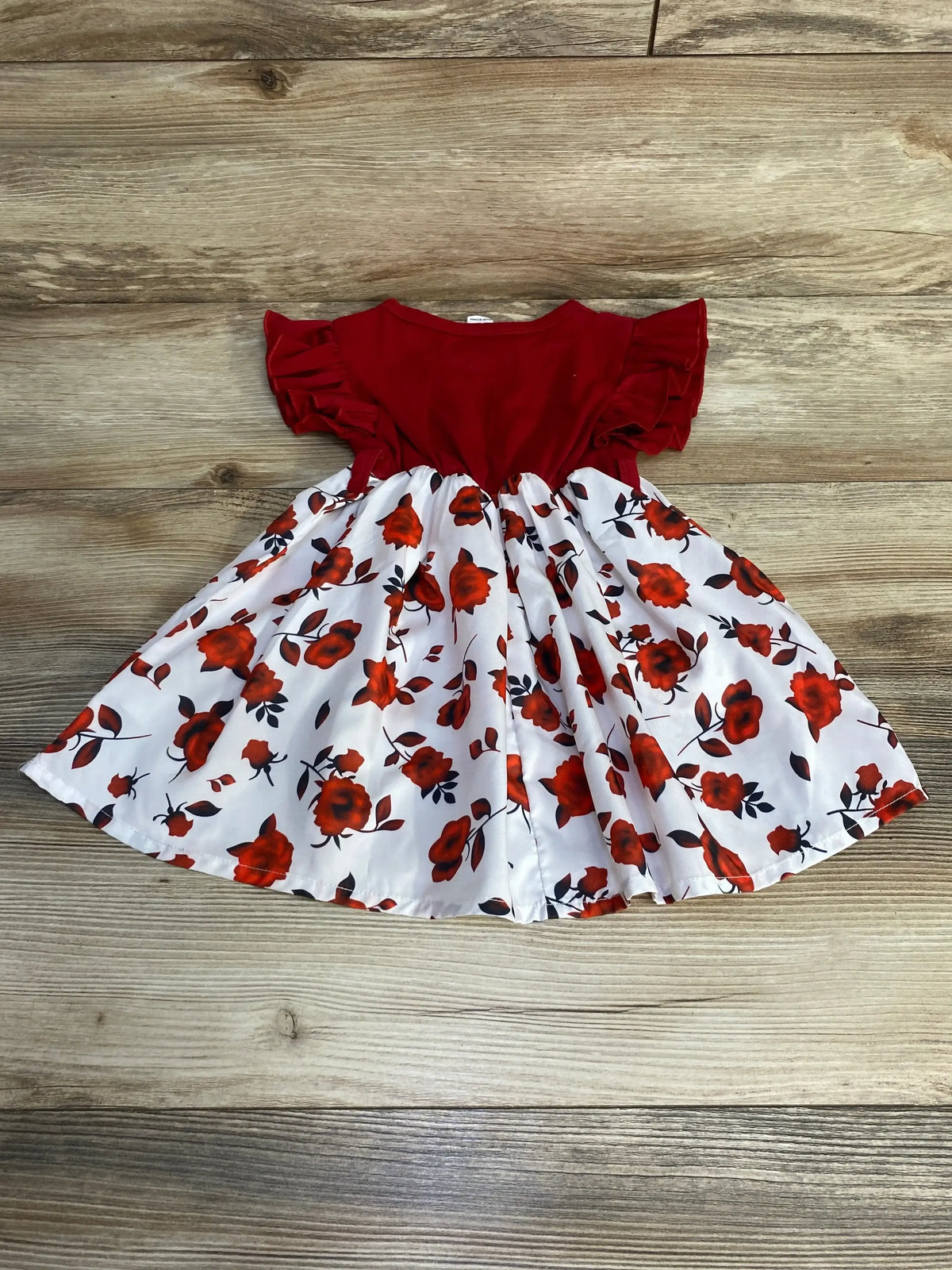 Flat lay of red top and white floral skirt baby dress (12-18 months) showing ruffled short sleeves and gathered skirt on wood background