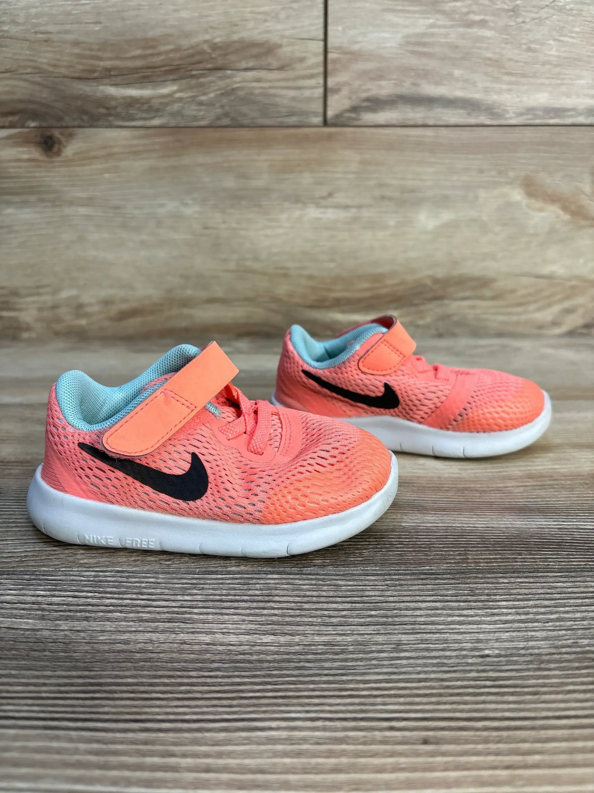 Coral Nike toddler shoes with Velcro straps and white soles on wood floor.