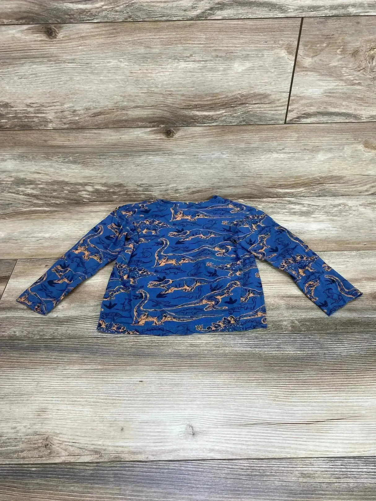 Flat lay of blue Craft + Flow long-sleeve toddler shirt size 4T showing orange dinosaur print on wood floor background