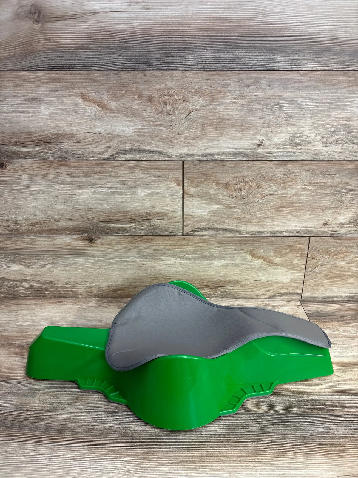 Three-quarter view of Crawligator tummy time toy in green showing removable gray padded support on wooden floor