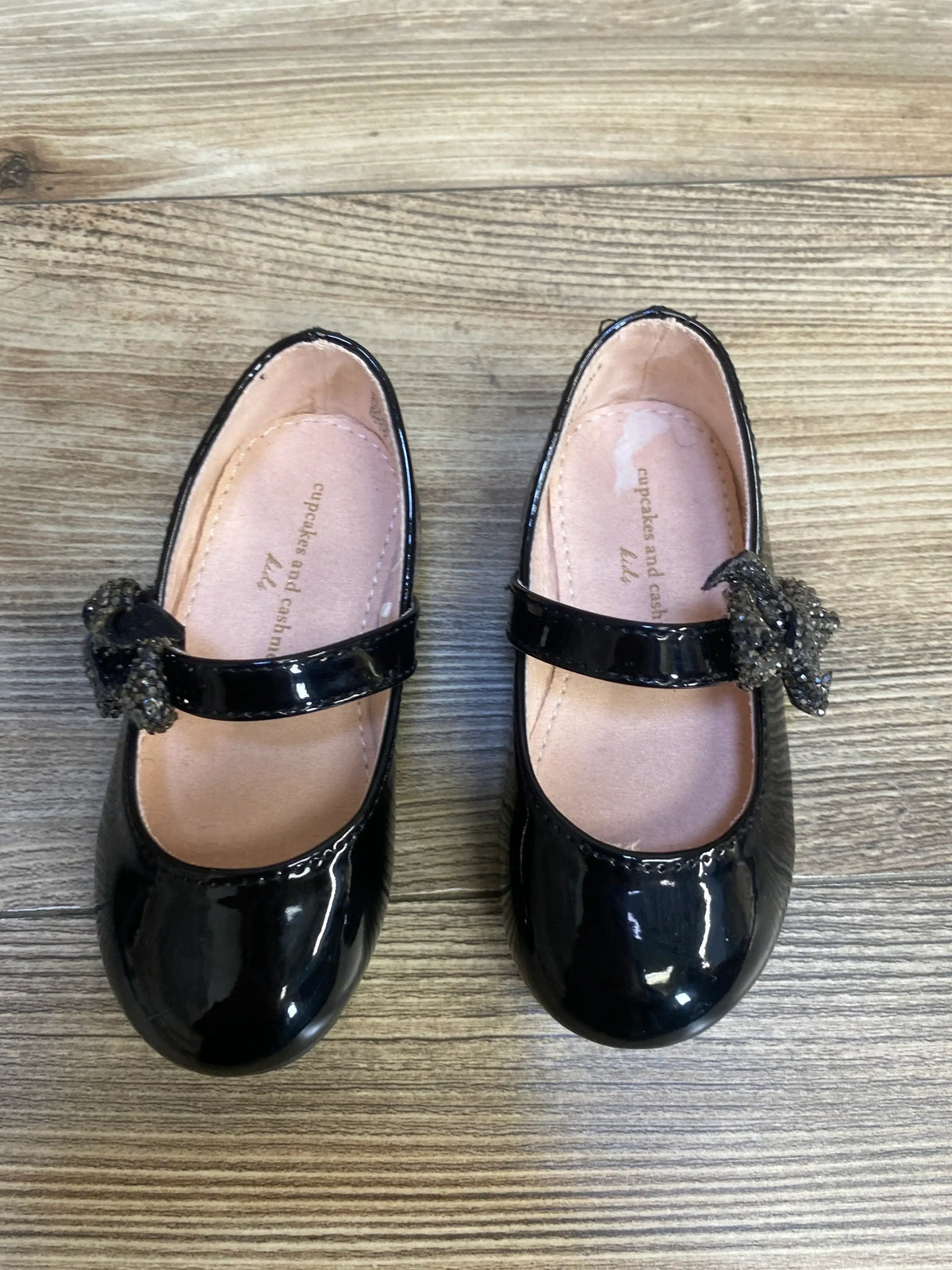 Black patent leather girls' dress shoes with bows, Mary Jane style, on wood floor
