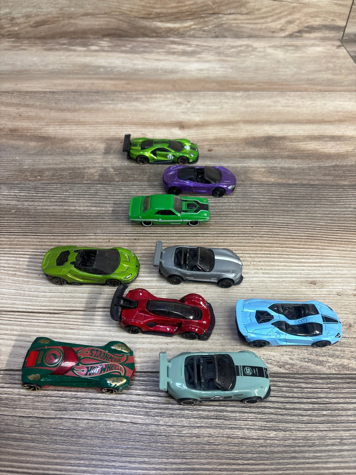 Nine miniature colorful Hot Wheels toy cars on wooden surface in various designs and colors