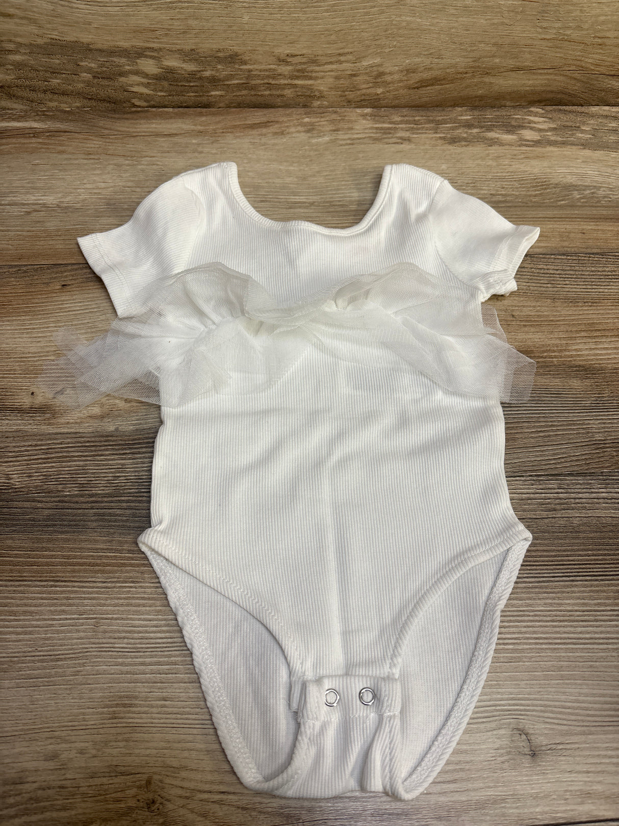 White baby onesie with ruffle tulle detail on wooden background