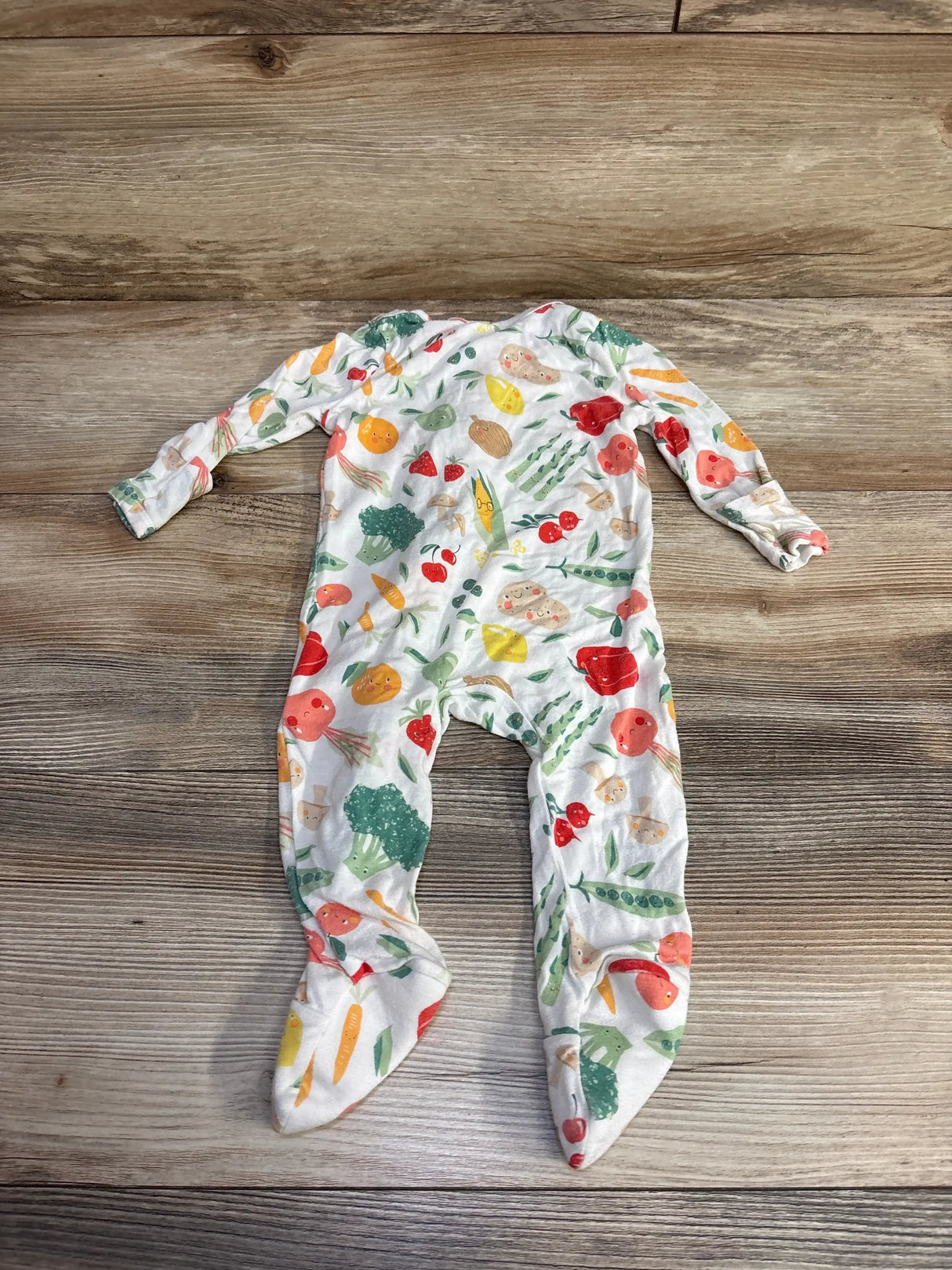 Top-down view of white Angel Dear footie with colorful vegetable print, long sleeves and built-in feet on wood background