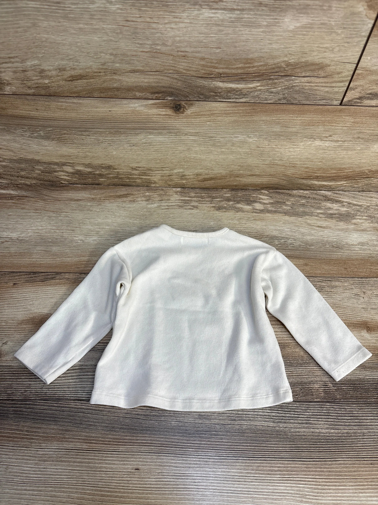 White long sleeve baby shirt on wood floor, kids clothing resale