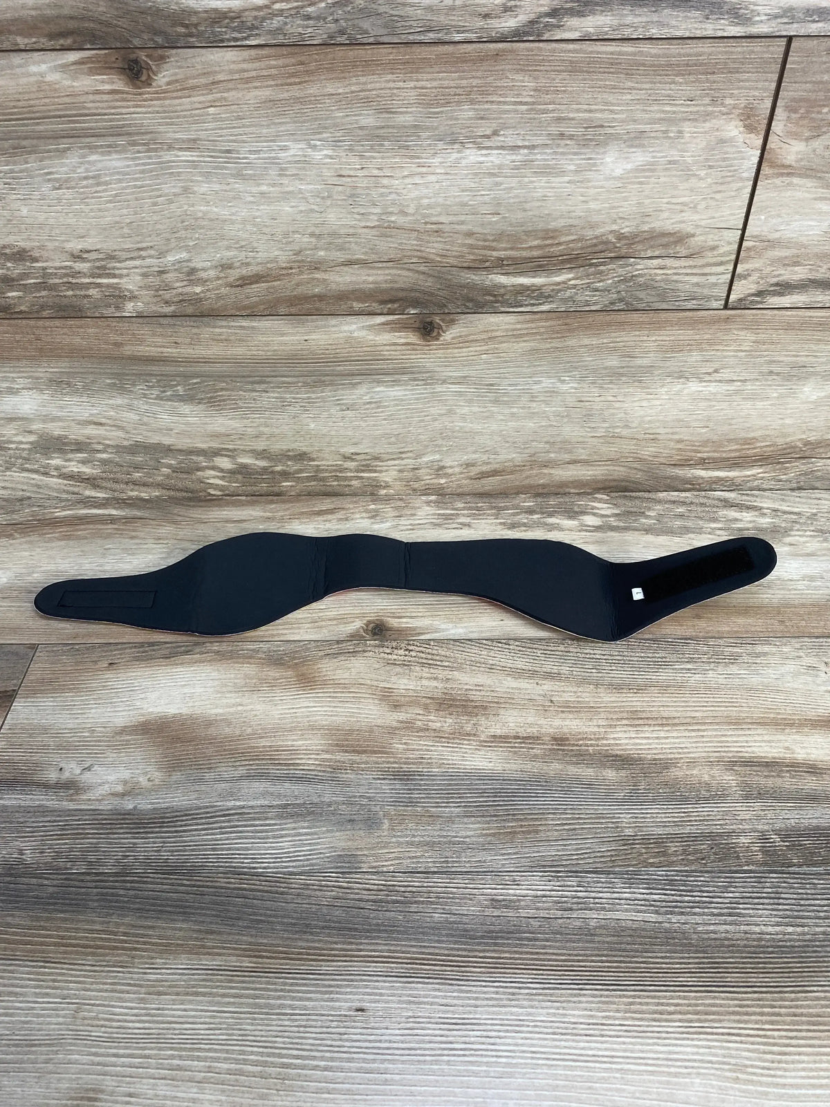 Flat lay of Ear Band-It Ultra swimming headband showcasing contoured ear covers and Velcro strap with wood floor background