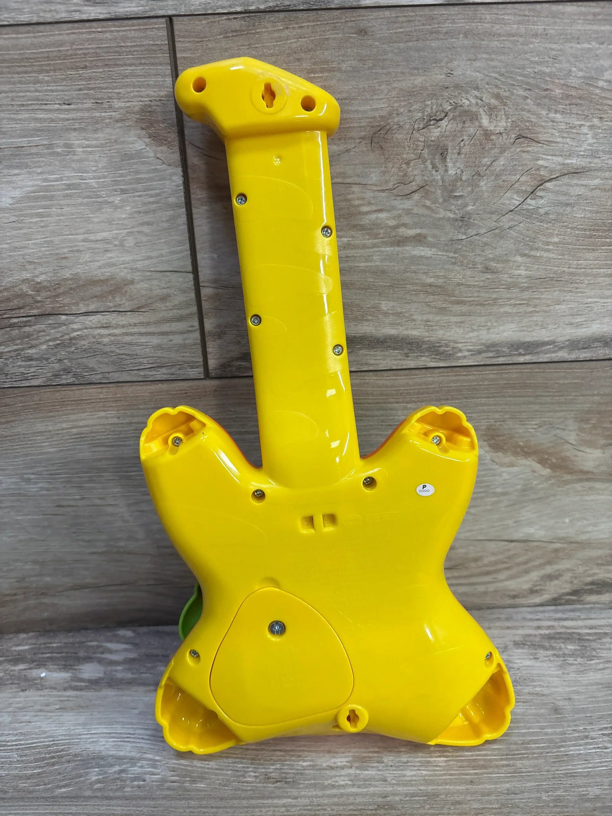 Back view of VTech Zoo Jamz Tiger Rock Guitar showcasing yellow casing, battery compartment, and power switch on wood floor