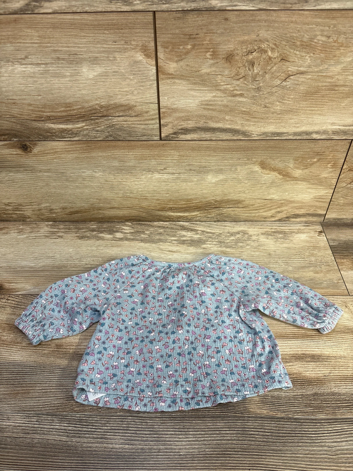 Flat lay of Carter's blue floral long-sleeve baby shirt size 3M showing gathered neckline and elasticized cuffs on wood background