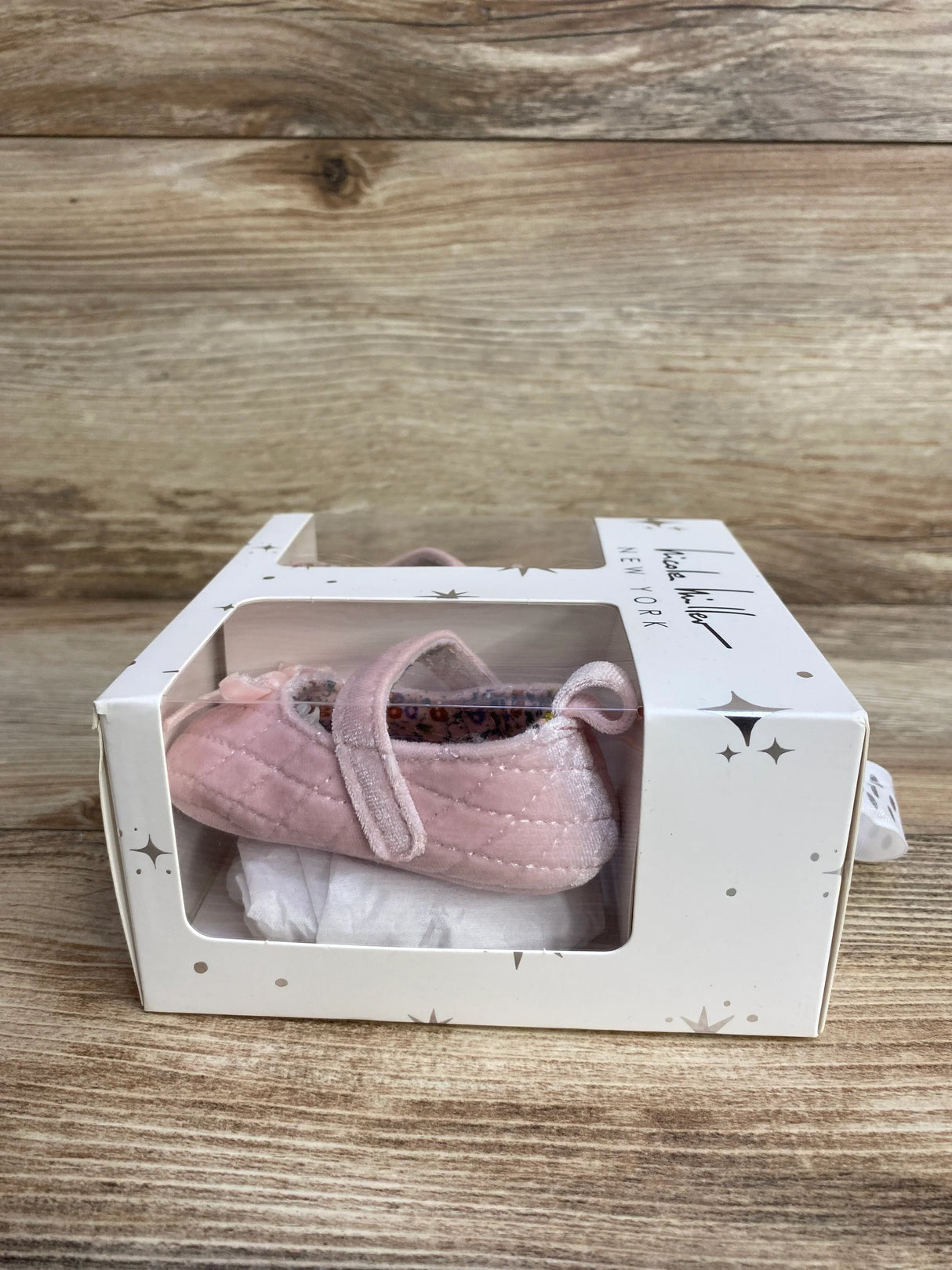 Pink quilted baby shoe with strap in gift box on wood background