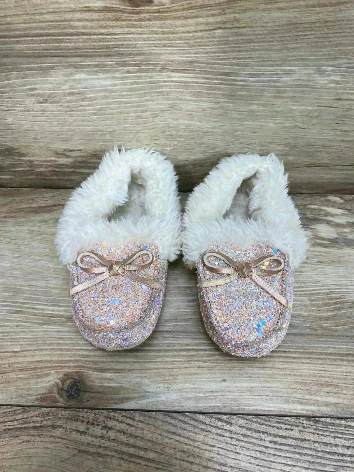 Top view of Cat & Jack toddler slippers with pink iridescent glitter, faux-fur lining, and bows on wood