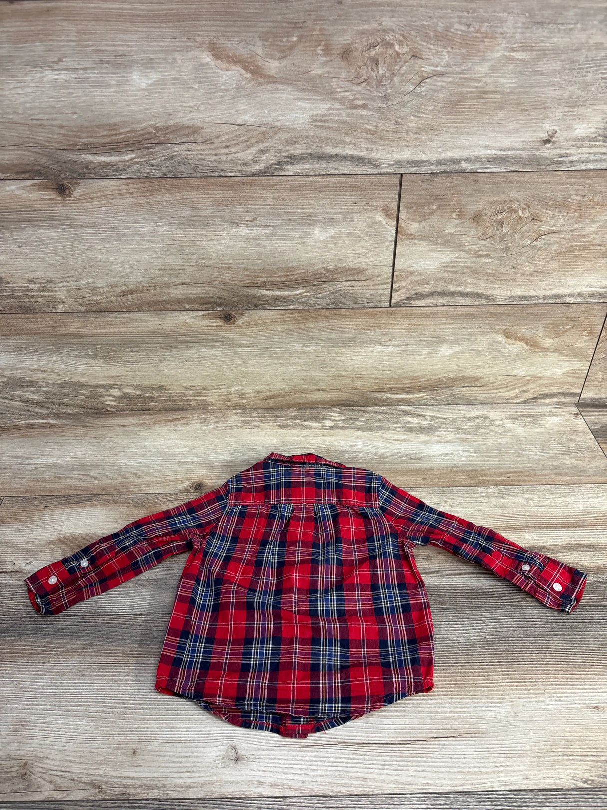 Back view of a red and navy plaid long-sleeve shirt for kids on wooden floor background