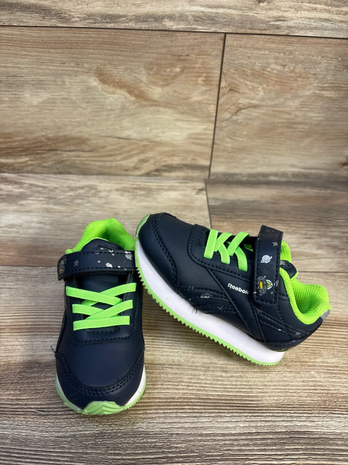 Front and side view of Reebok Space Sneakers showcasing navy and green details with hook and loop closures on a wood-grain floor