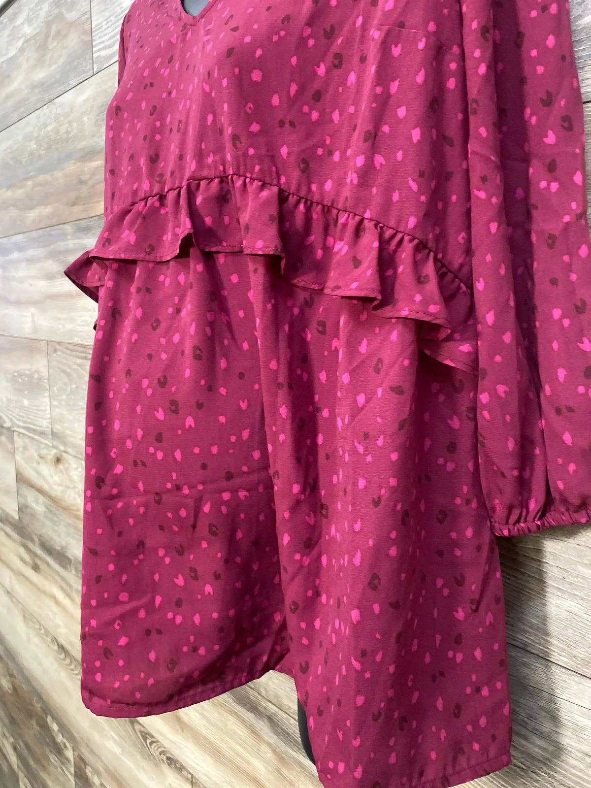 Close up front of Isabel maternity woven top in berry showing ruffle waist and pink spotted print against wood plank backdrop