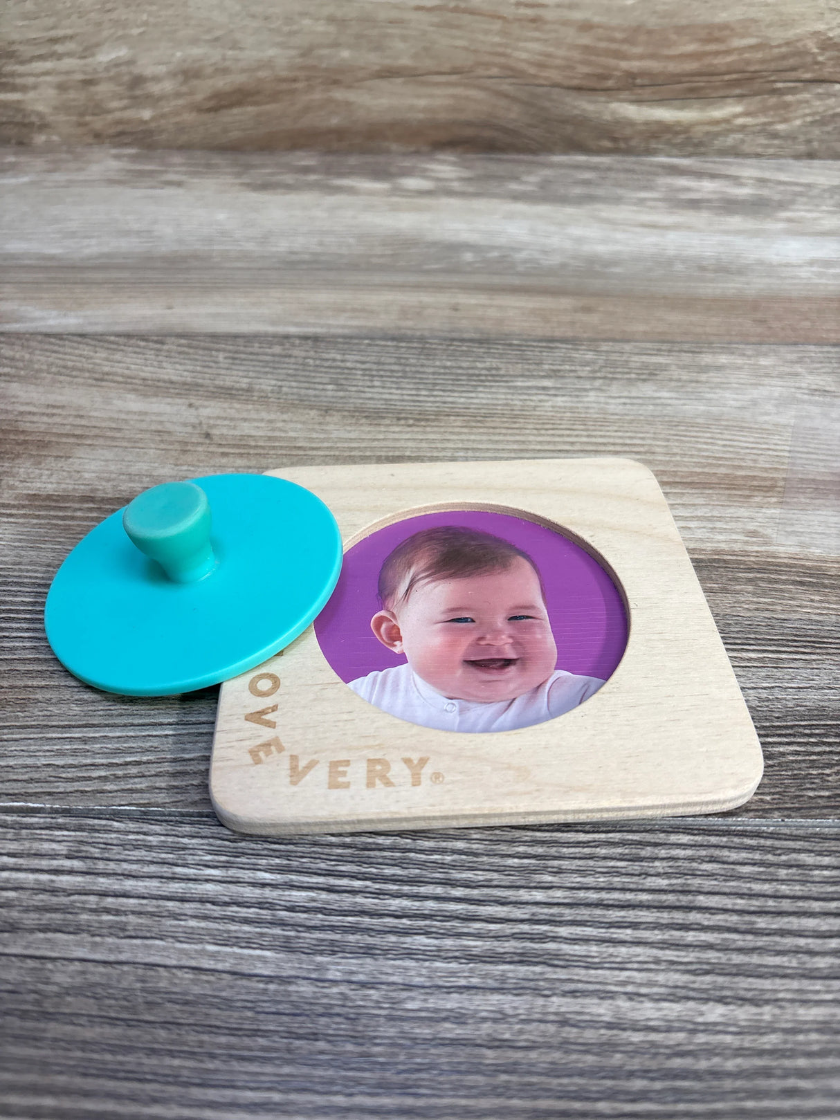 Lovevery wooden baby puzzle with round blue knob and smiling infant photo on wood surface
