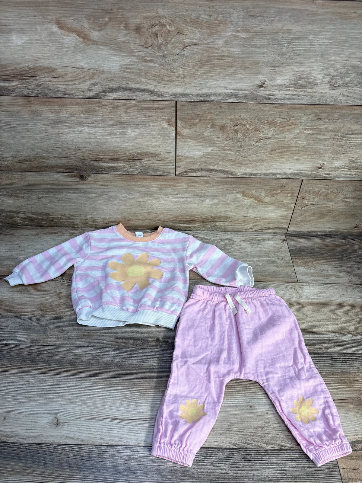 Flat lay of Old Navy pink two piece sweatshirt and joggers set showcasing striped sweatshirt and flower accents on a wood floor