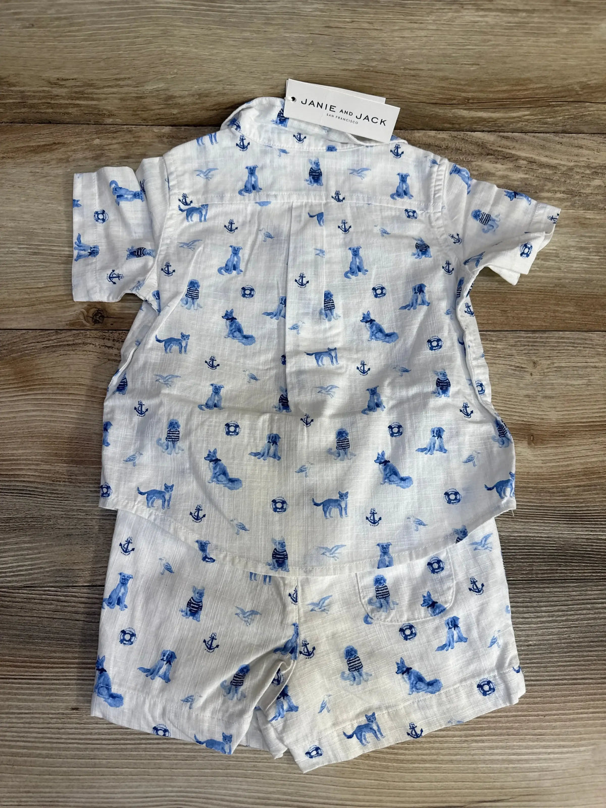 Top-down view of Janie & Jack cabana set showcasing blue nautical toile, chest pocket, and matching shorts on wood background