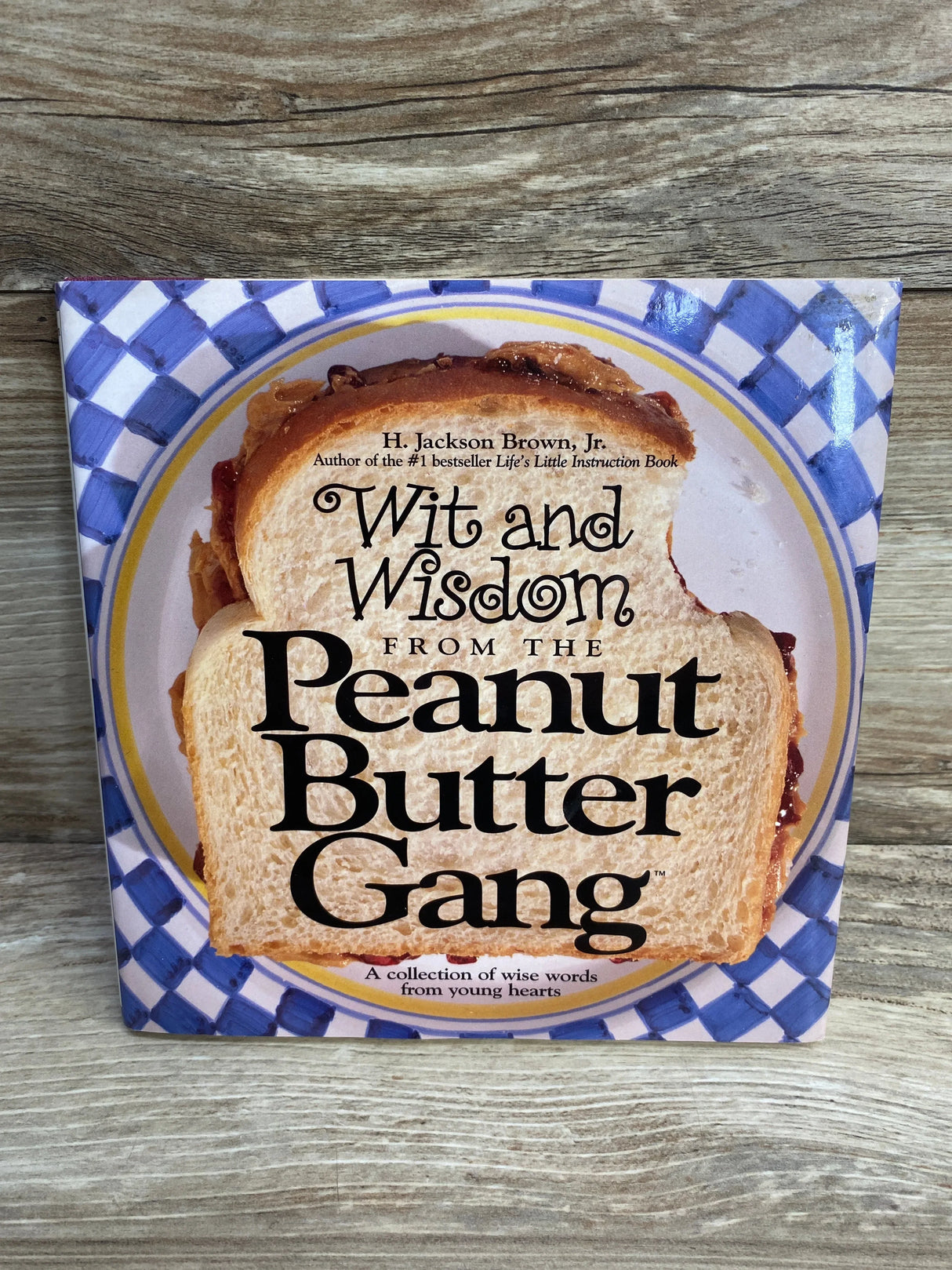 Front cover of Wit and Wisdom from the Peanut Butter Gang hardcover showing a sandwich on a blue-checkered plate on wood