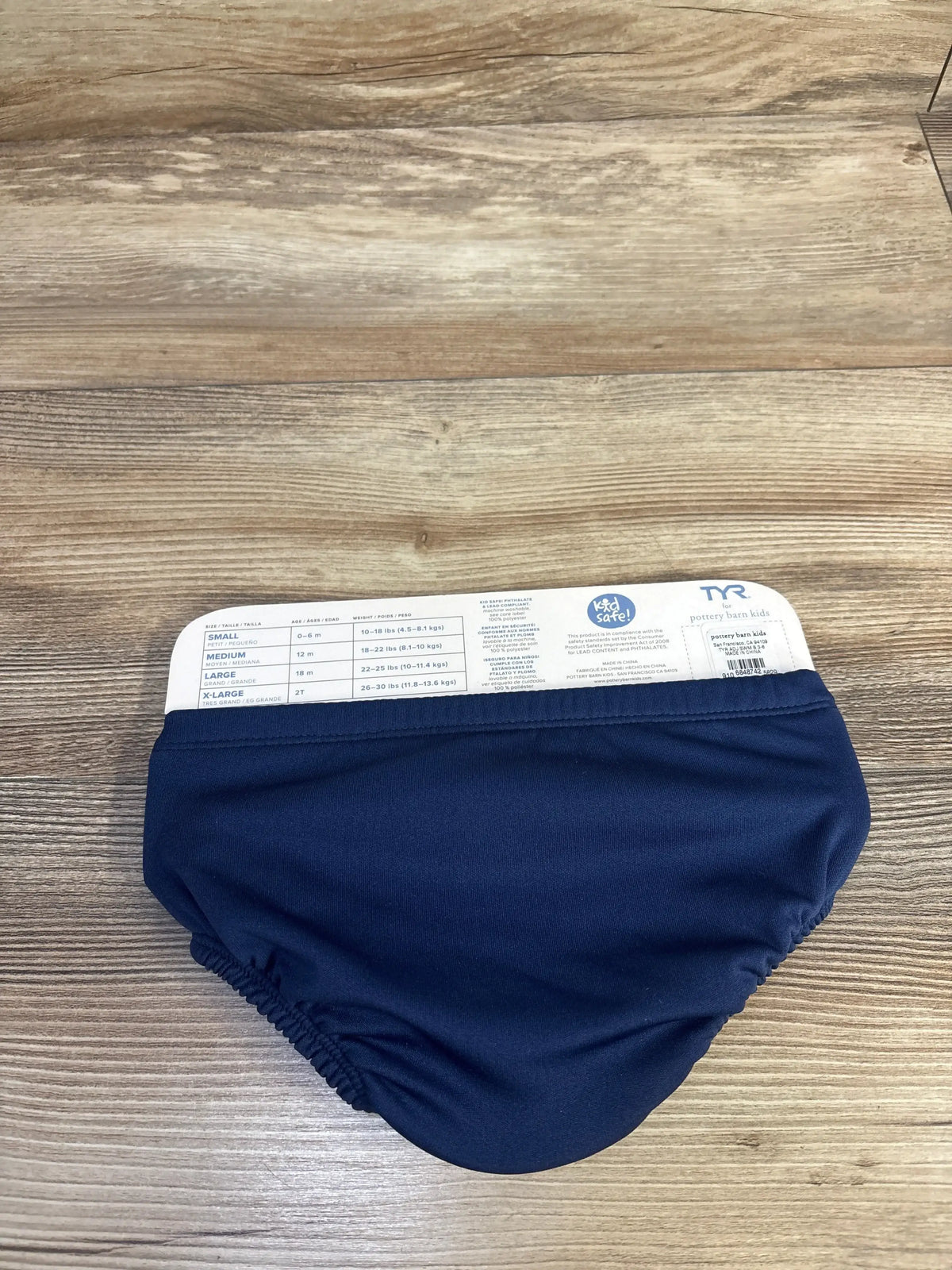 Front view of navy Pottery Barn baby swim diaper, size small 0-6 months, with gathered elastic openings on wood surface