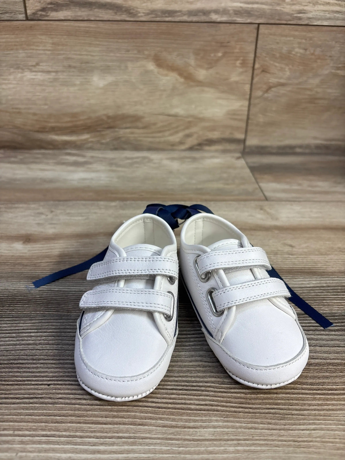 Front view of white Janie & Jack toddler sneakers, size 3/4C, showcasing double strap closures on a wood-look floor