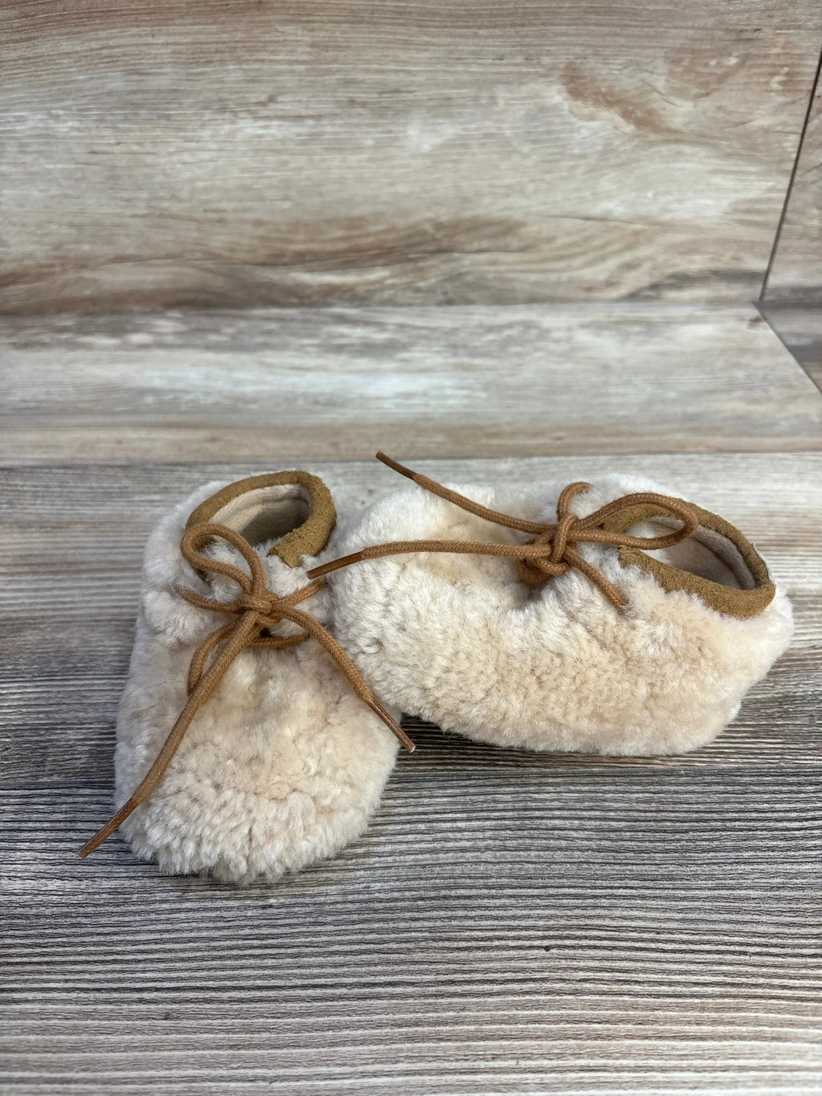 Cream shearling baby booties with tan laces on rustic wooden background