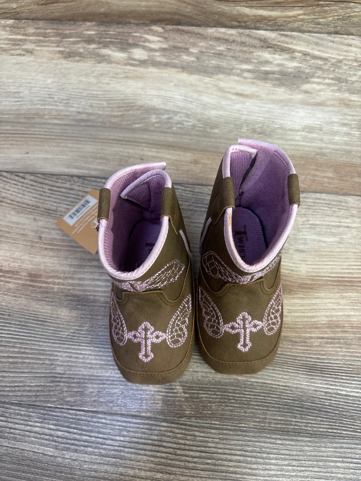 Top-down of Twister Gracie baby bucker boots, brown faux-suede with pink embroidery and pink lining on wood floor