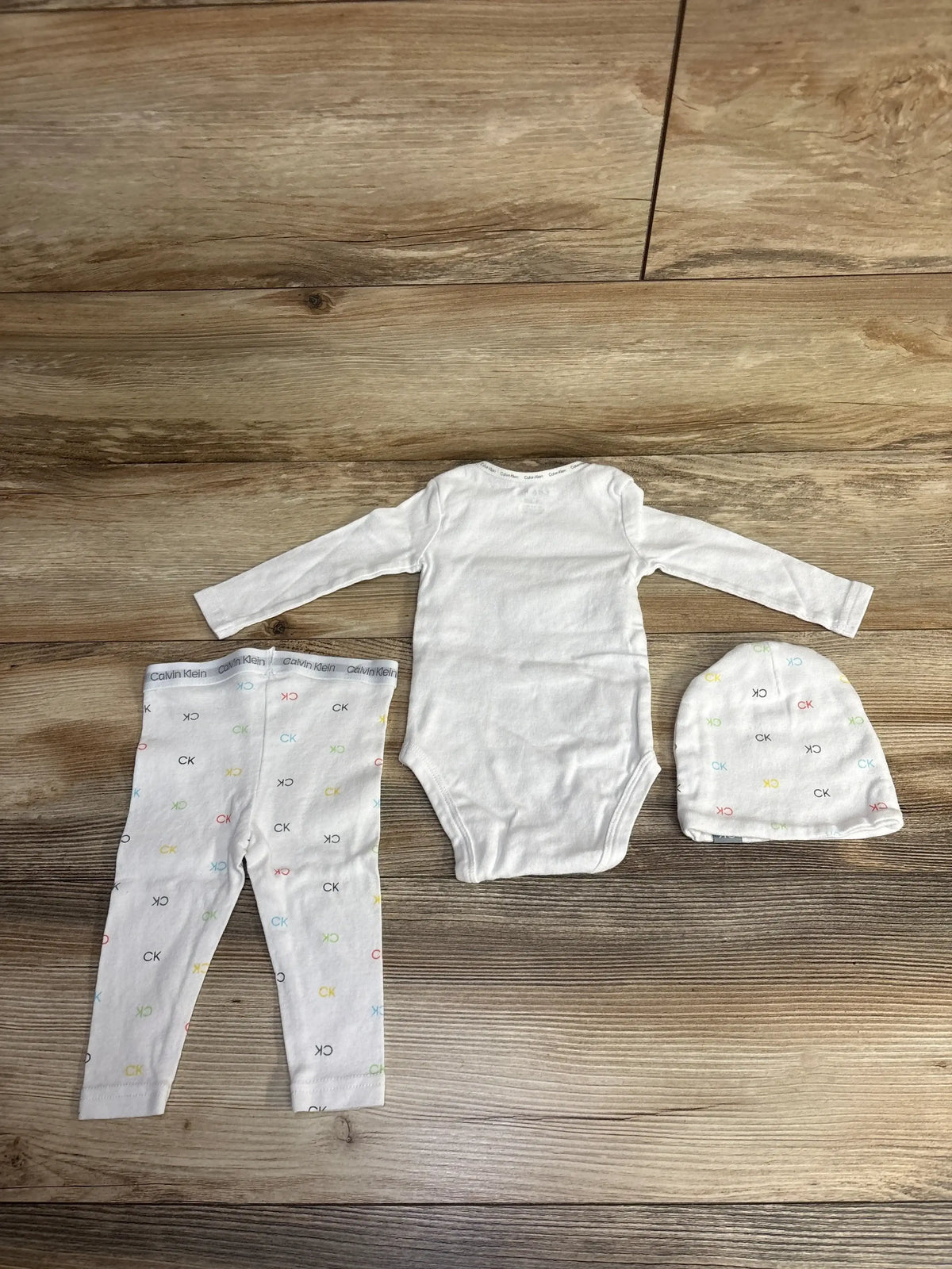 White baby outfit set with long sleeve bodysuit, printed pants, and matching hat on wood floor